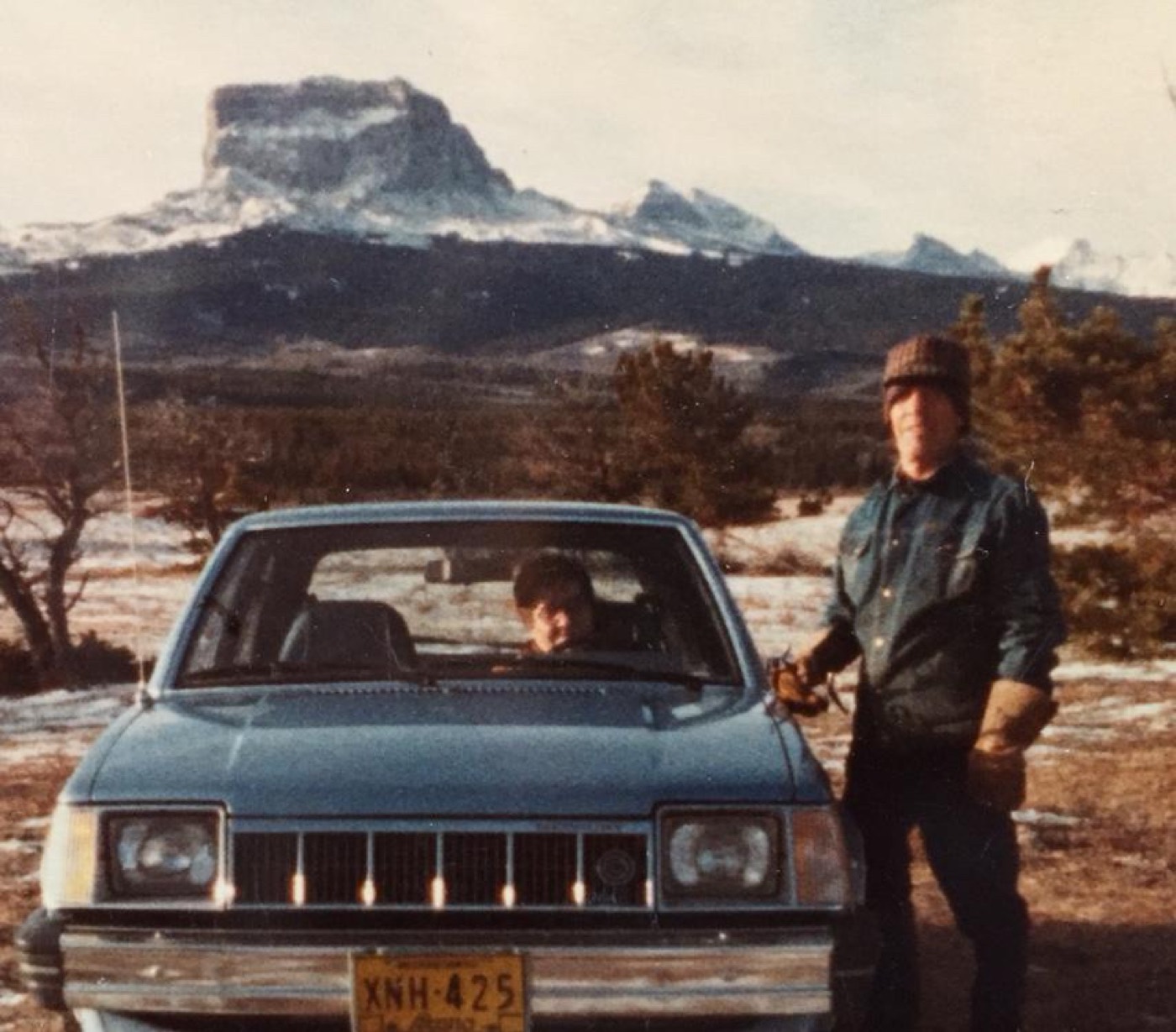 A faded photograph of a man and a boy beside a blue car, with Chief Mountain behind them